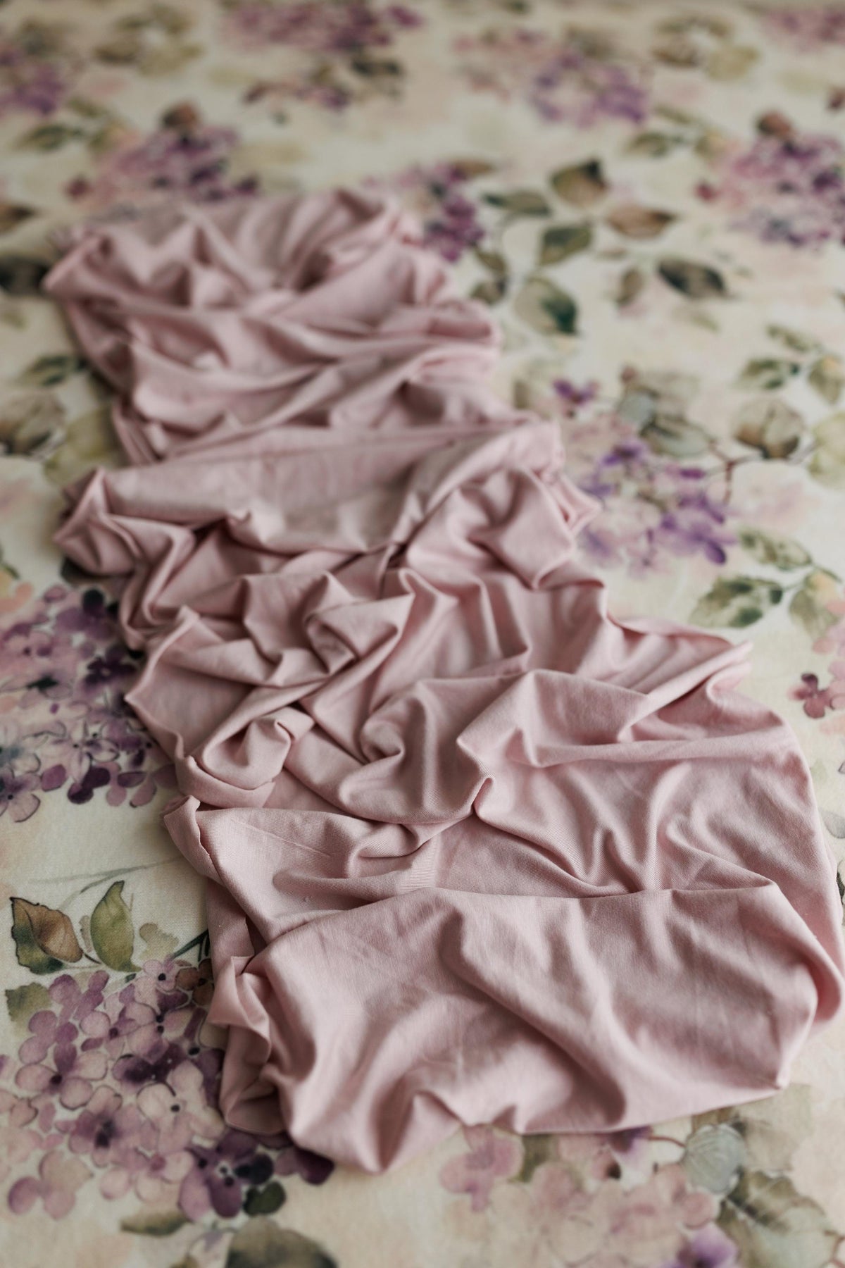 Mauve jersey fabric draped over a creamy floral watercolor posing backdrop.