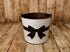 Midnight Bow newborn photography bucket cover featuring a large black satin-style bow and matching ribbon on a textured white background, displayed on a rustic metal posing bucket with a wooden farmhouse backdrop.
