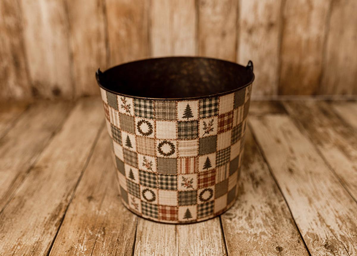 Christmas Scraps newborn photography bucket cover featuring vintage Christmas patchwork squares with evergreen trees, wreaths, rustic plaid, ticking stripes, and botanical details in muted reds, greens, and warm creams, displayed on a metal posing bucket.