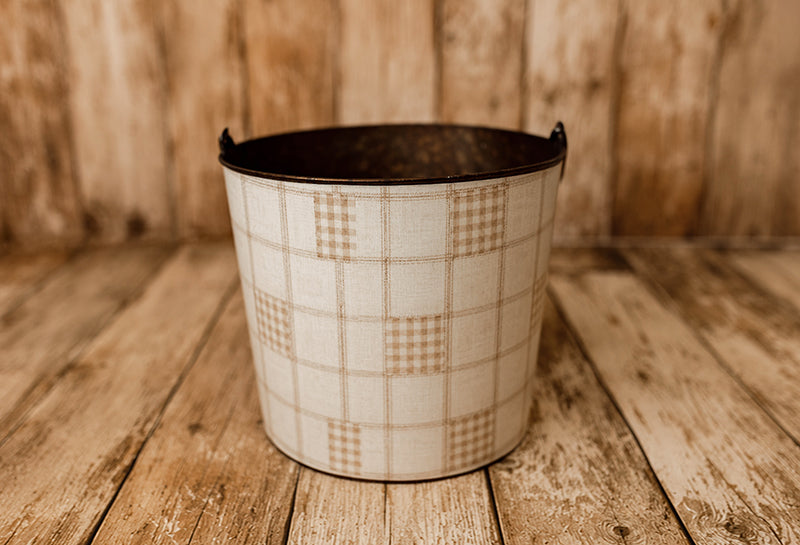 Grandpa's Twin newborn photography bucket cover featuring a vintage-inspired beige and cream plaid patchwork design with soft gingham checks and subtle linen texture, displayed on a rustic metal posing bucket.