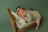 Newborn sleeping on a sage green stretch knit posing fabric backdrop in a rustic wooden bed with floral bedding.