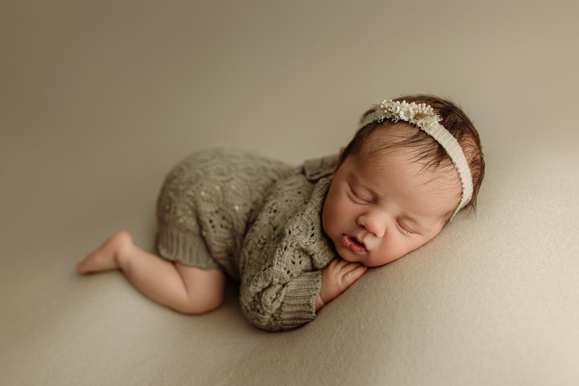 Newborn wearing a taupe open-knit romper with delicate texture, styled for a photography session.