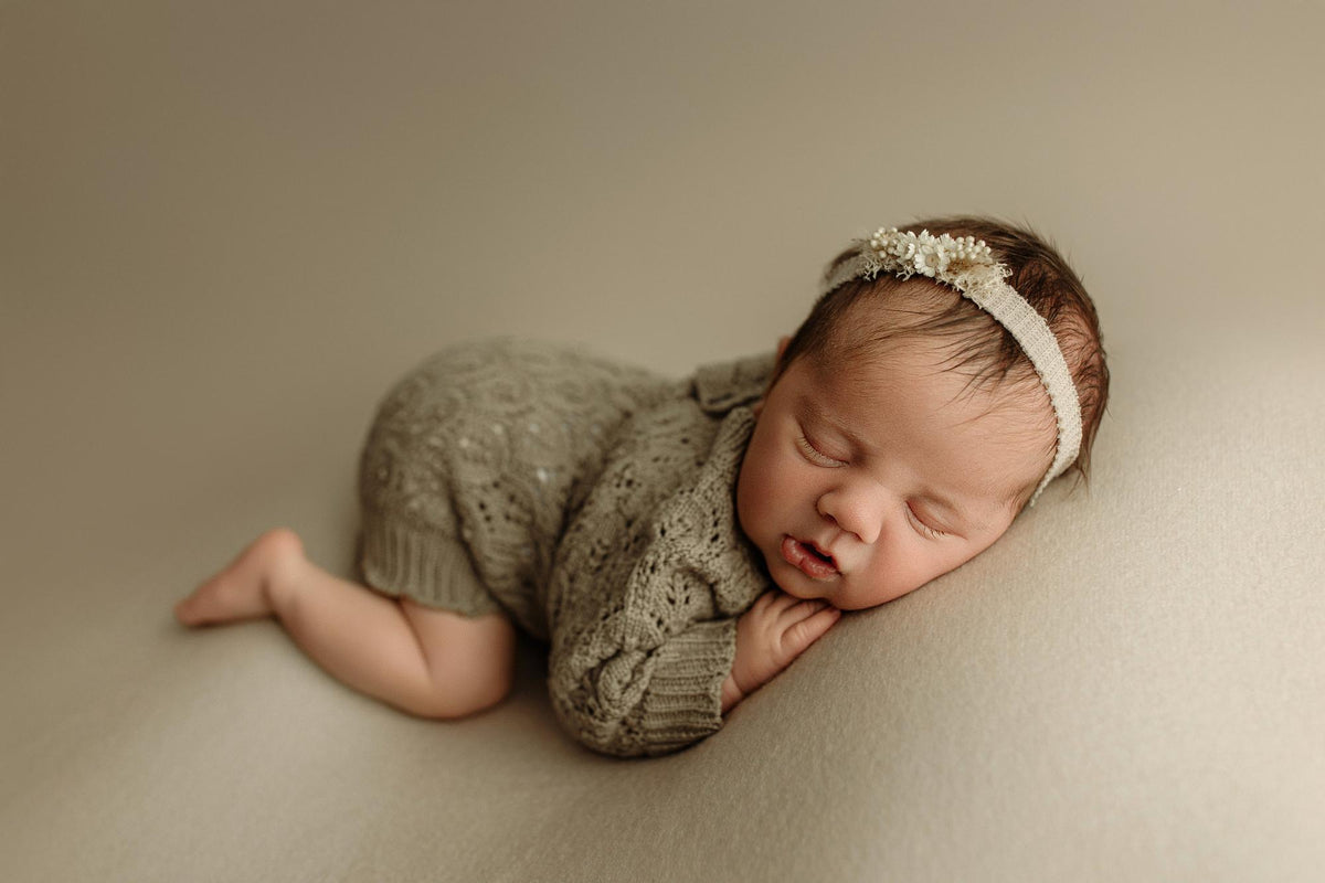 Newborn wearing a taupe open-knit romper with delicate texture, styled for a photography session.