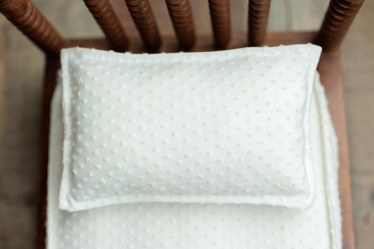 Ivory dobby cotton bedding set with a delicate dotted texture on a small wooden prop chair.