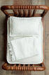 Ivory textured newborn wrap with delicate pattern, styled on a wooden bed prop.