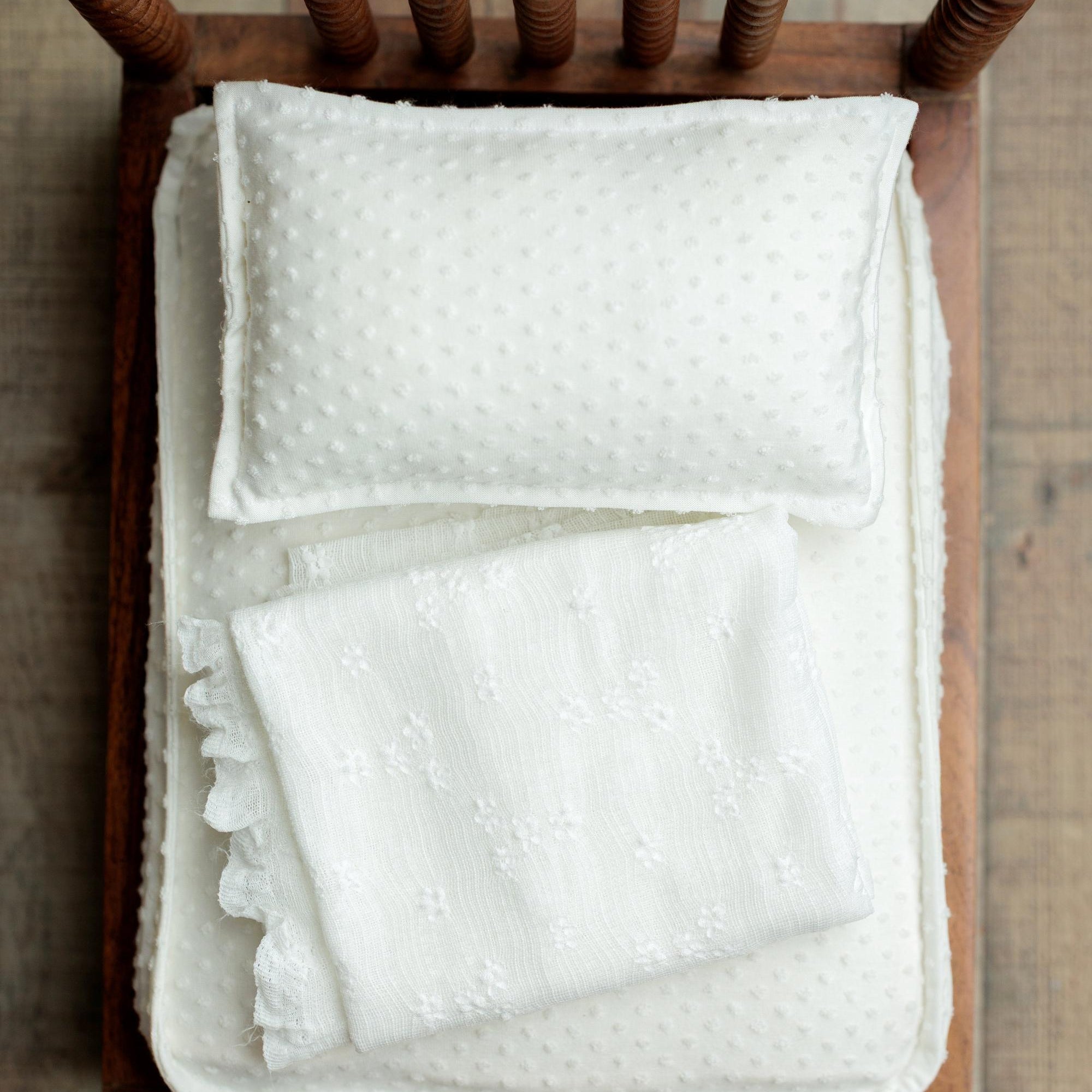 Ivory textured newborn wrap with delicate pattern, styled on a wooden bed prop.