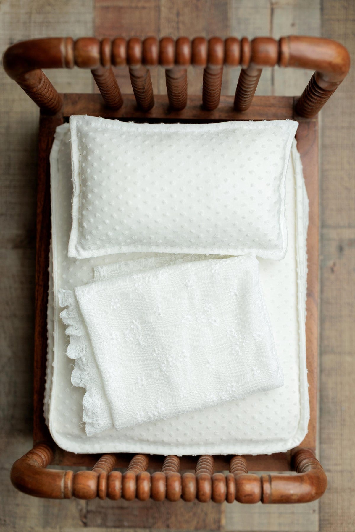 Ivory textured newborn wrap with delicate pattern, styled on a wooden bed prop.