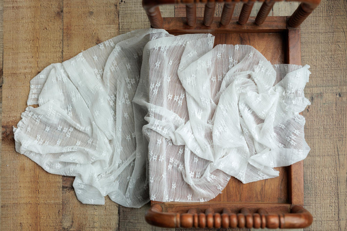 Ivory textured wrap with delicate floral pattern draped over a vintage wooden newborn photography bed.