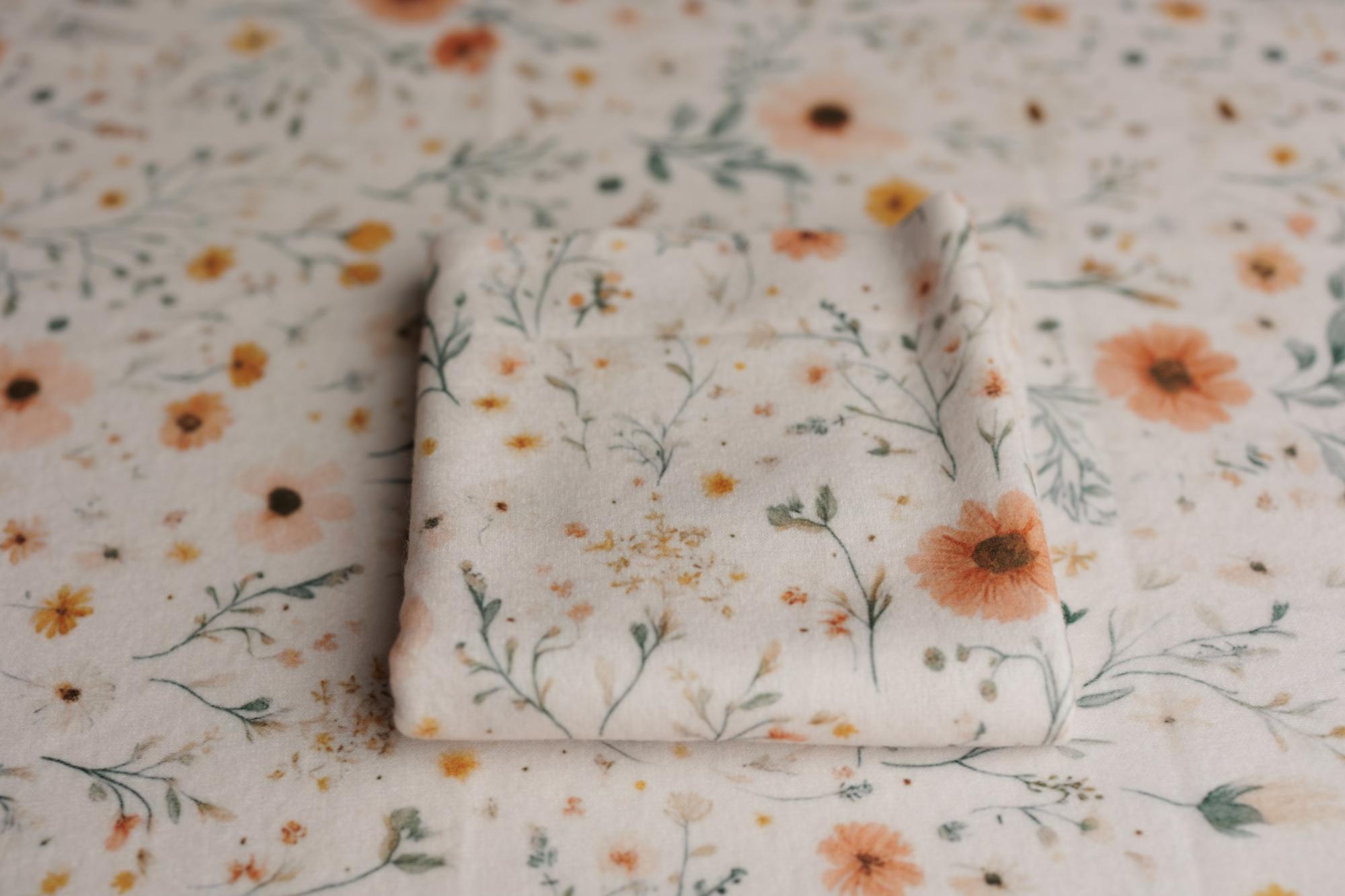 Newborn posing fabric and wrap featuring a delicate floral print in soft peach, gold, and sage tones on a cream background.