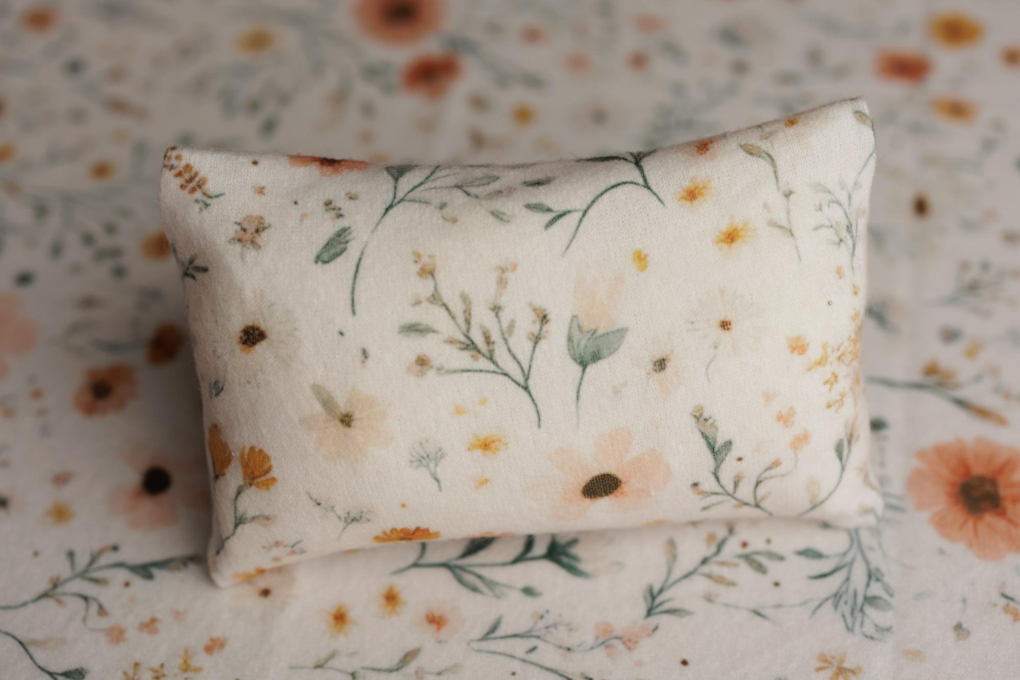 Small rectangular newborn photography pillow in a cream fabric with peach, gold, and sage floral print.