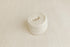 A rolled cream-colored knit blanket or fabric piece, shown on a matching textured cream background.