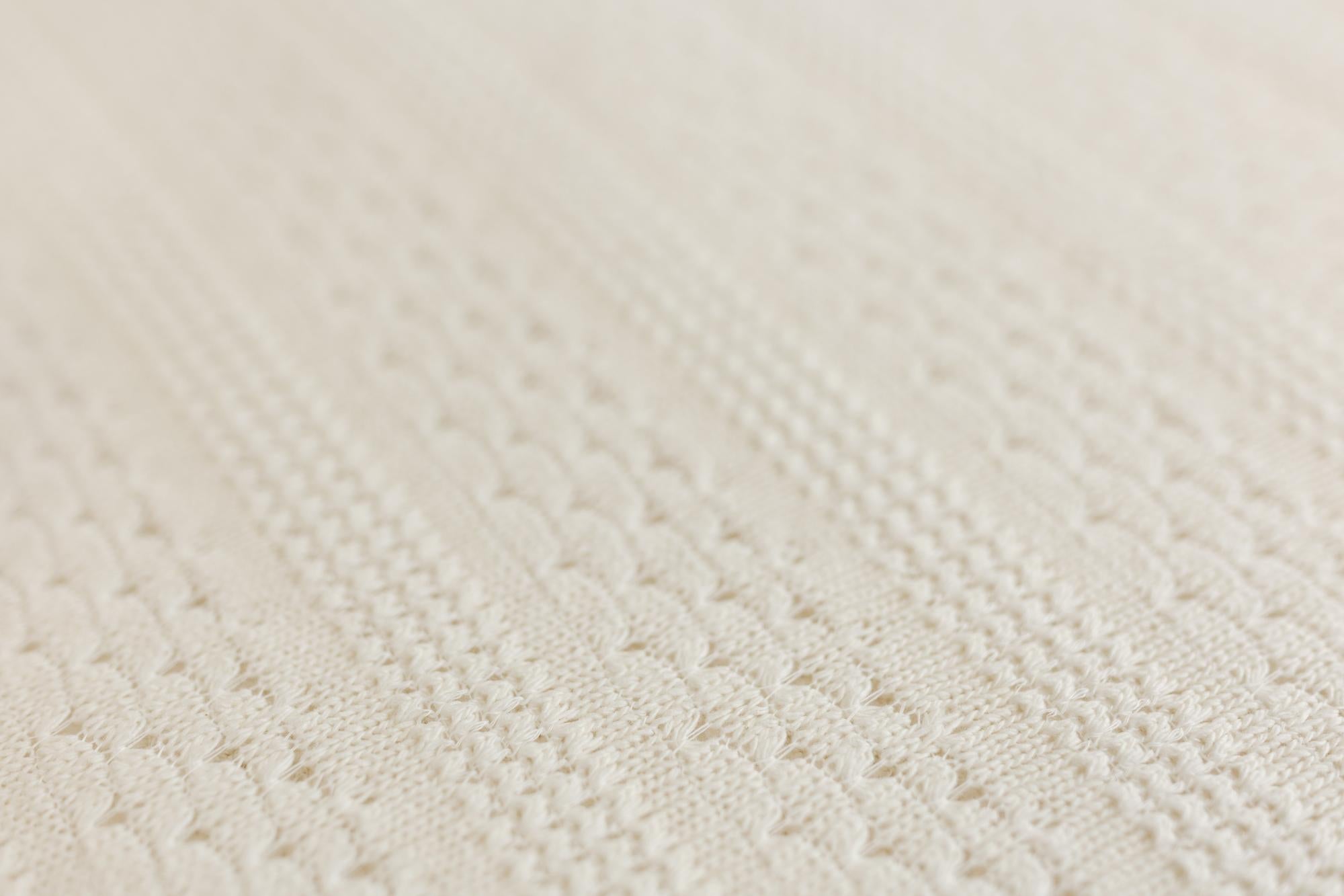 Close-up of a cream-colored textured knit fabric with a fine cable-knit pattern.
