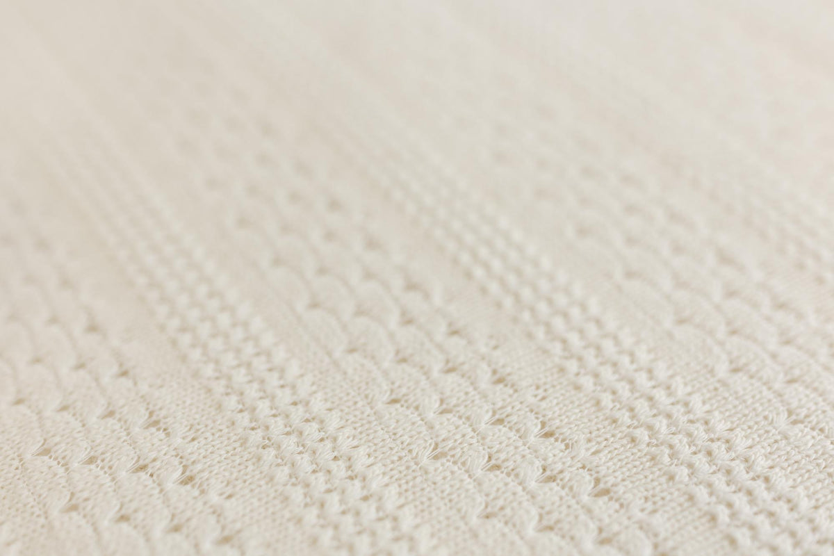 Close-up of a cream-colored textured knit fabric with a fine cable-knit pattern.