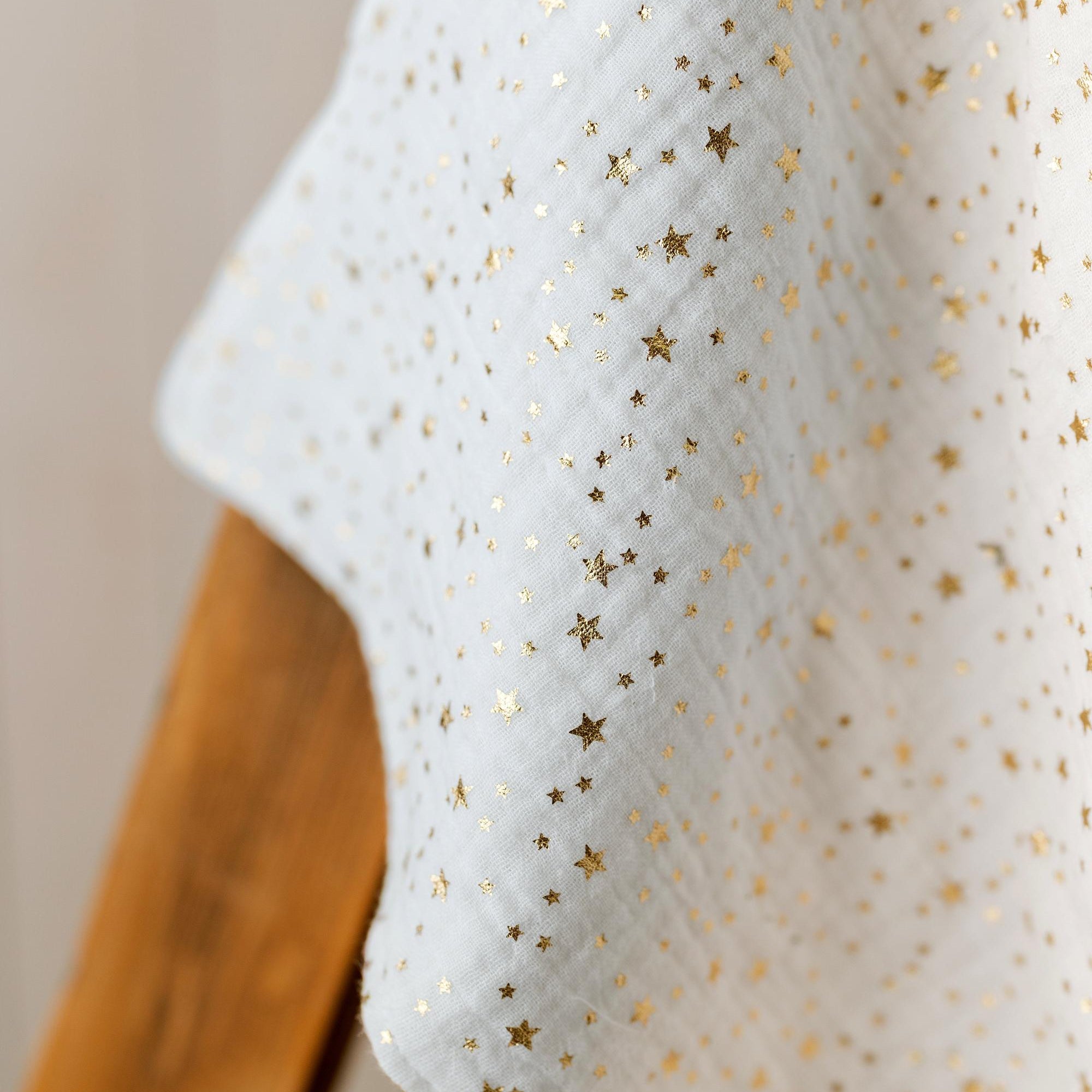 White muslin fabric with a scattered gold foil star pattern, draped over a wooden surface.