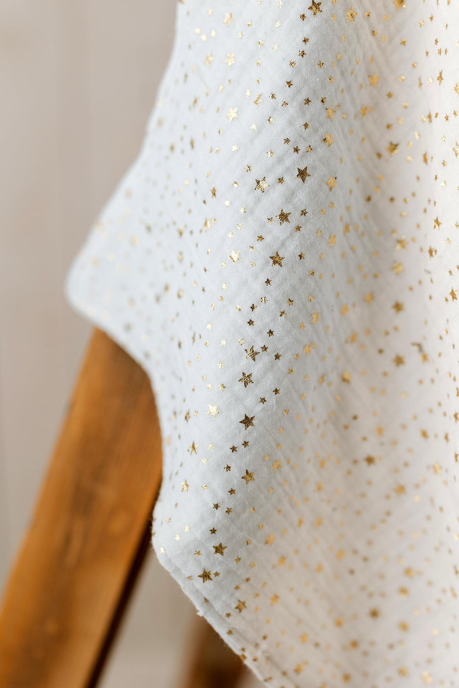 White muslin fabric with a scattered gold foil star pattern, draped over a wooden surface.