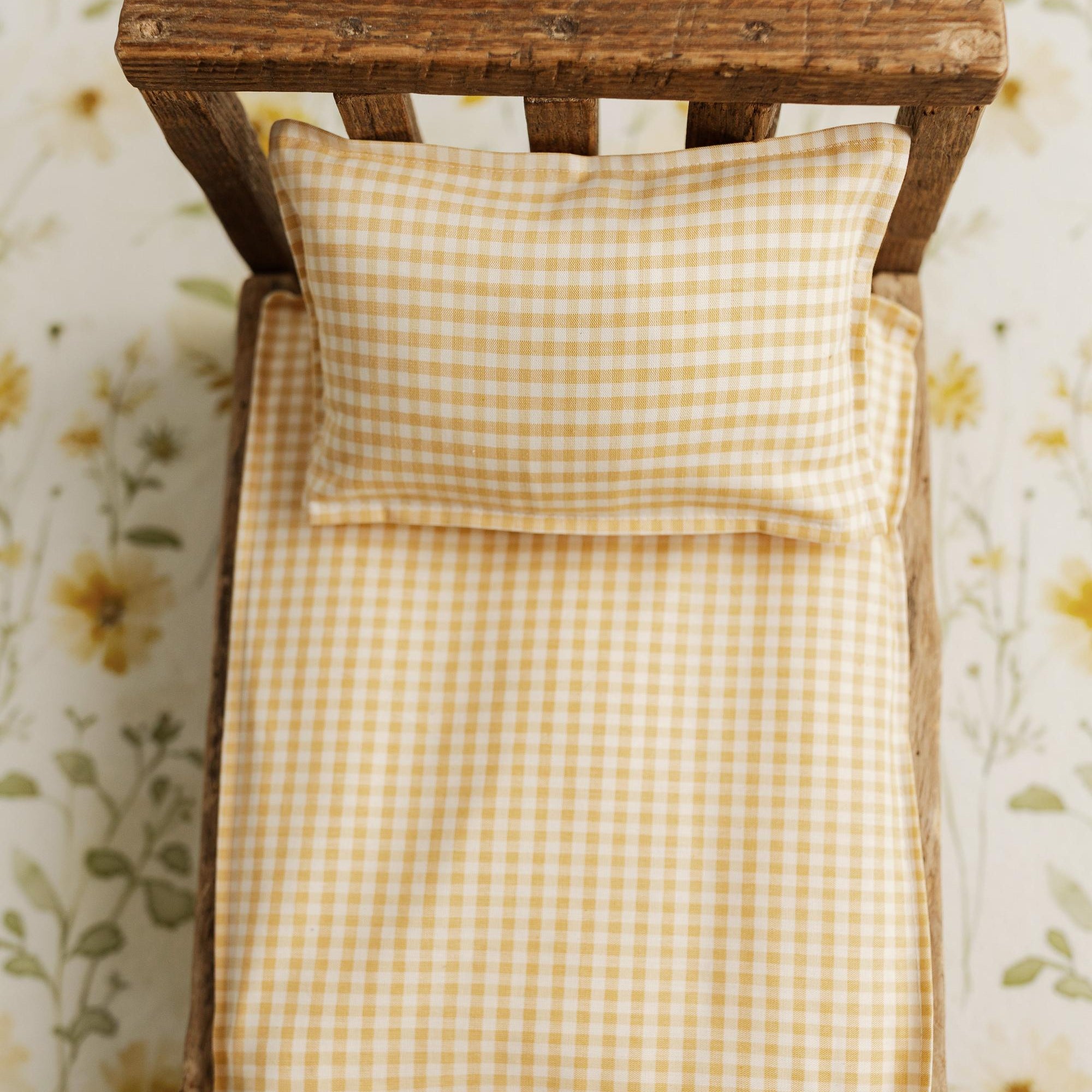 Butter yellow gingham newborn photography bed sheet and matching pillowcase set on a rustic wooden prop bed.