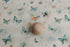 Creamy neutral newborn posing fabric with sage, teal, and peach butterfly prints and a smooth wooden sphere prop.