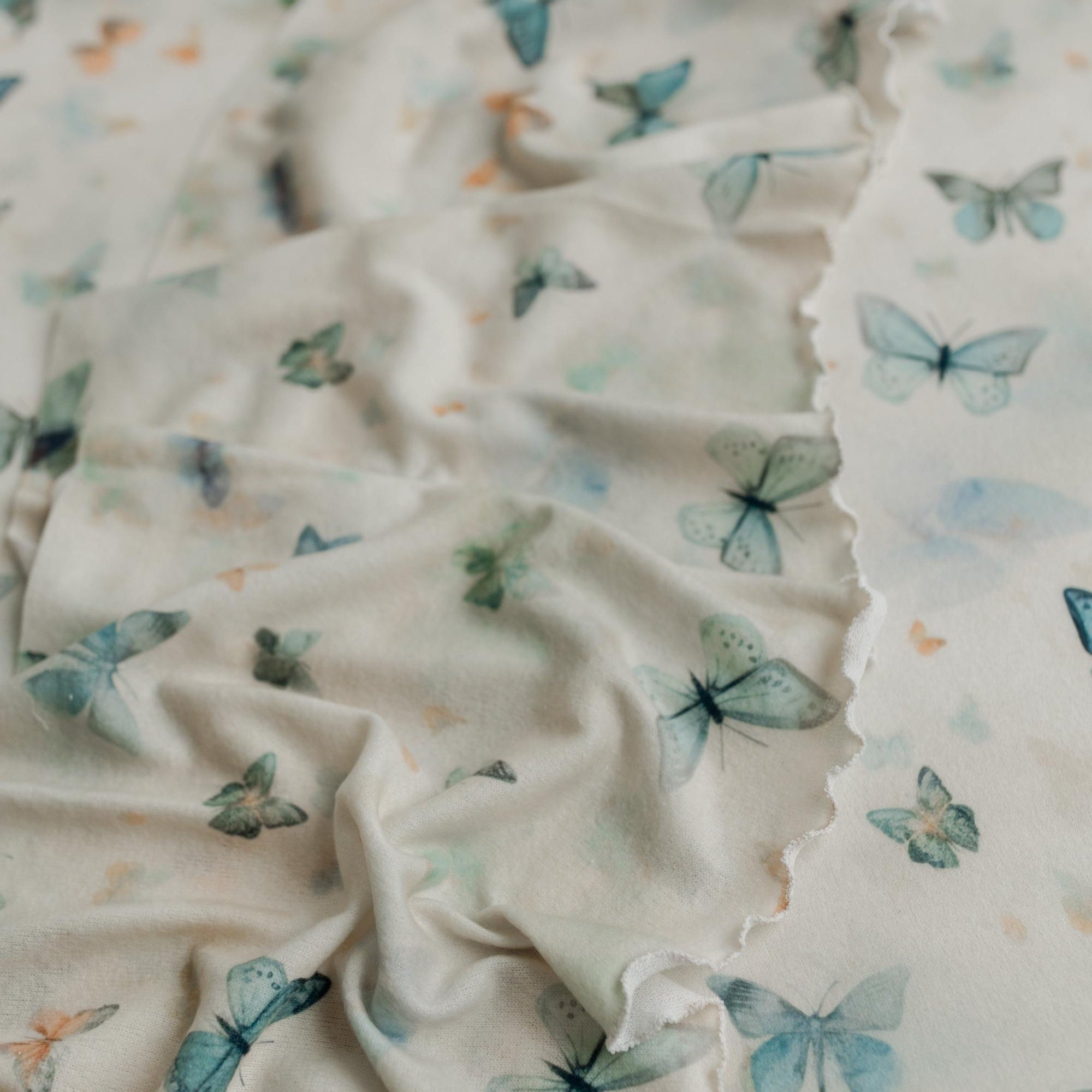 Soft cream knit posing fabric with a whimsical butterfly print in muted sage, teal, and peach tones for newborn photography.