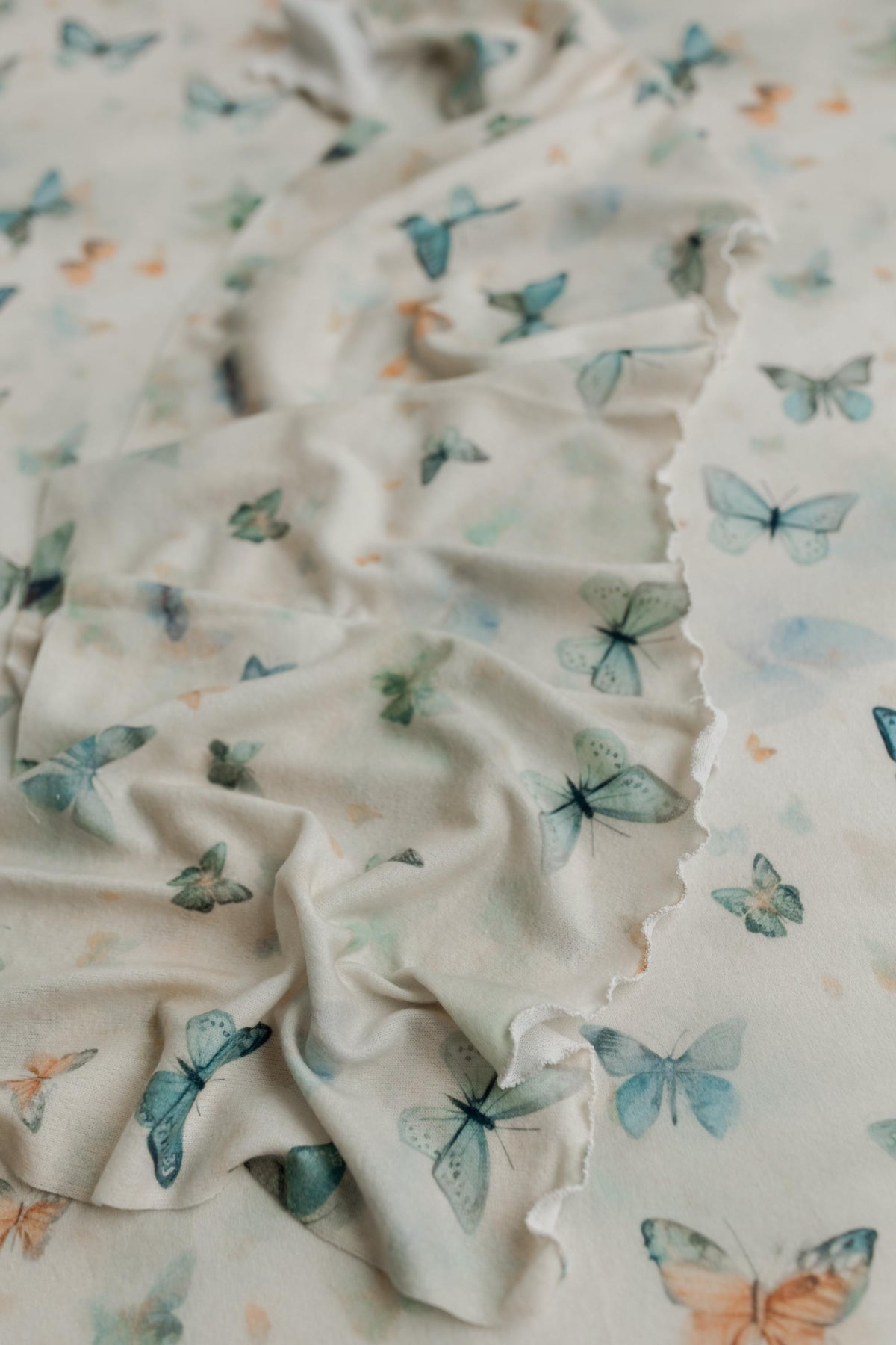 Soft cream knit posing fabric with a whimsical butterfly print in muted sage, teal, and peach tones for newborn photography.