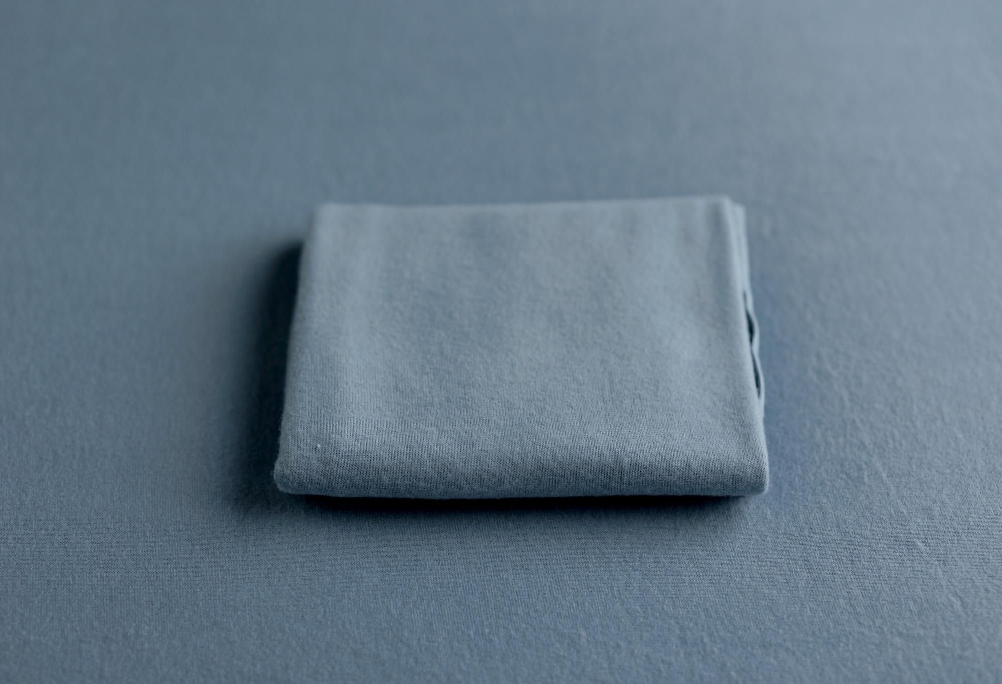 Folded deep dusty blue cashmere-style wrap with a soft, matte texture on a matching fabric background.
