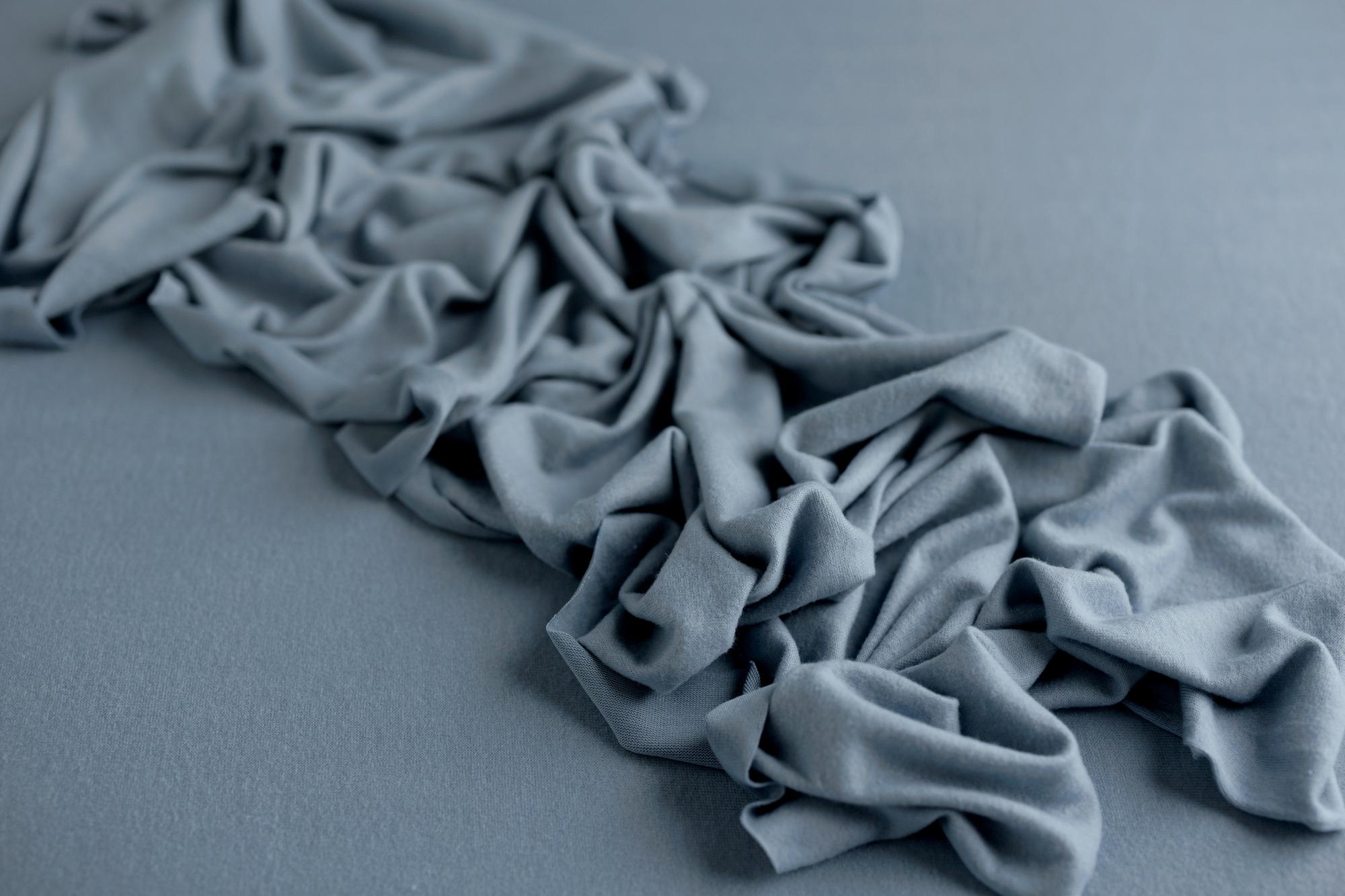 Deep dusty blue cashmere-style wrap featuring soft, draped fabric folds on a matching textured background.