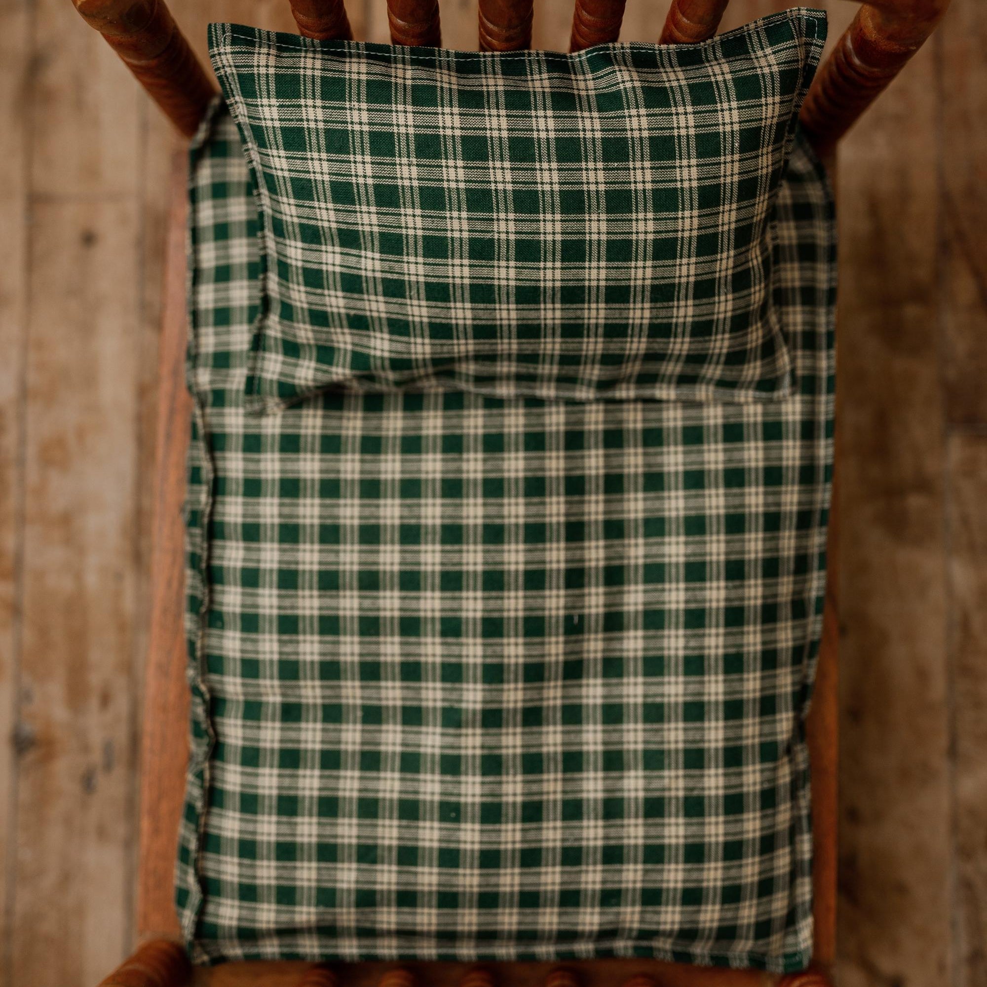 Newborn photography bed set featuring a forest green and cream plaid sheet and matching pillowcase on a wooden bed.