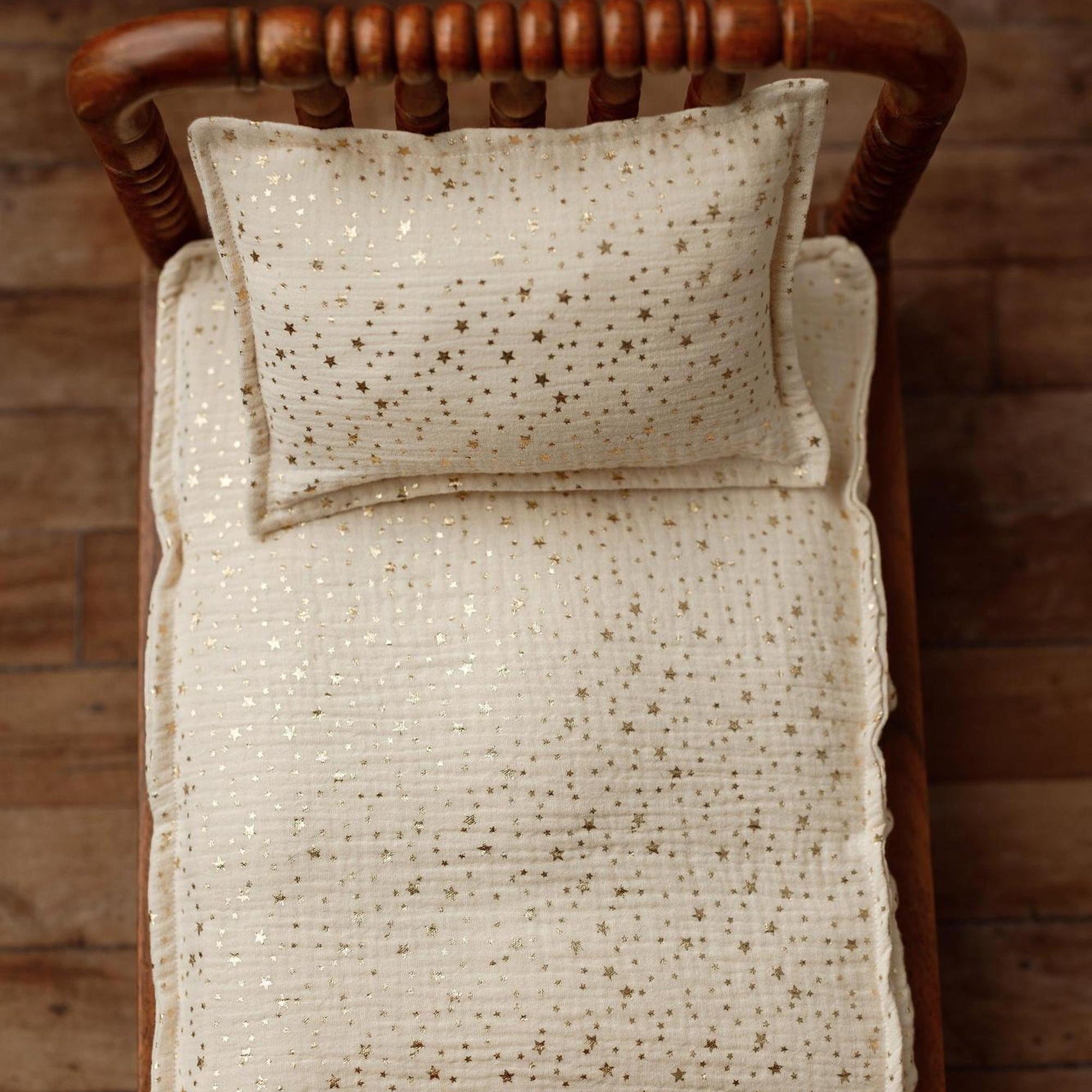 Ivory newborn photography mattress sheet and pillowcase set featuring a metallic gold star pattern on a wooden bed.