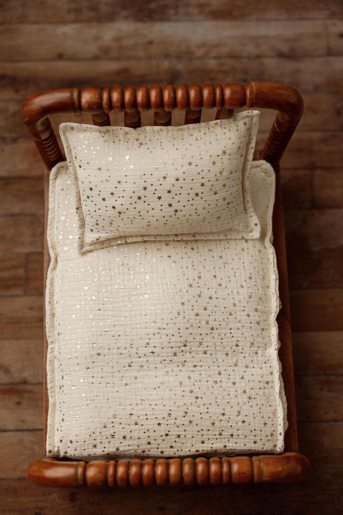 Ivory newborn photography mattress sheet and pillowcase set featuring a metallic gold star pattern on a wooden bed.