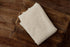 Beige, open-knit newborn photography fabric wrap with a textured, ramen-toned finish folded on a rustic wooden crate.