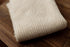 Folded beige ramen-toned newborn photography fabric with a soft, open-knit texture resting on a dark wooden surface.