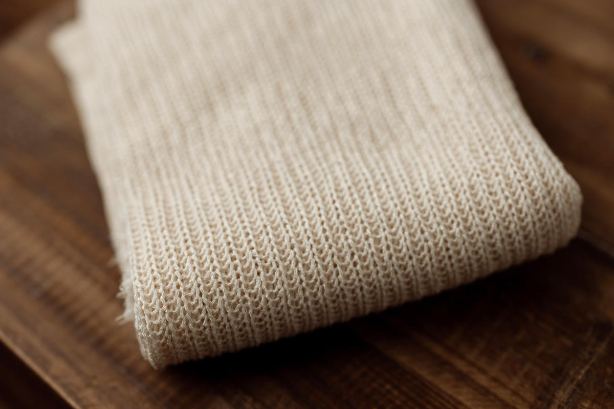 Folded beige ramen-toned newborn photography fabric with a soft, open-knit texture resting on a dark wooden surface.
