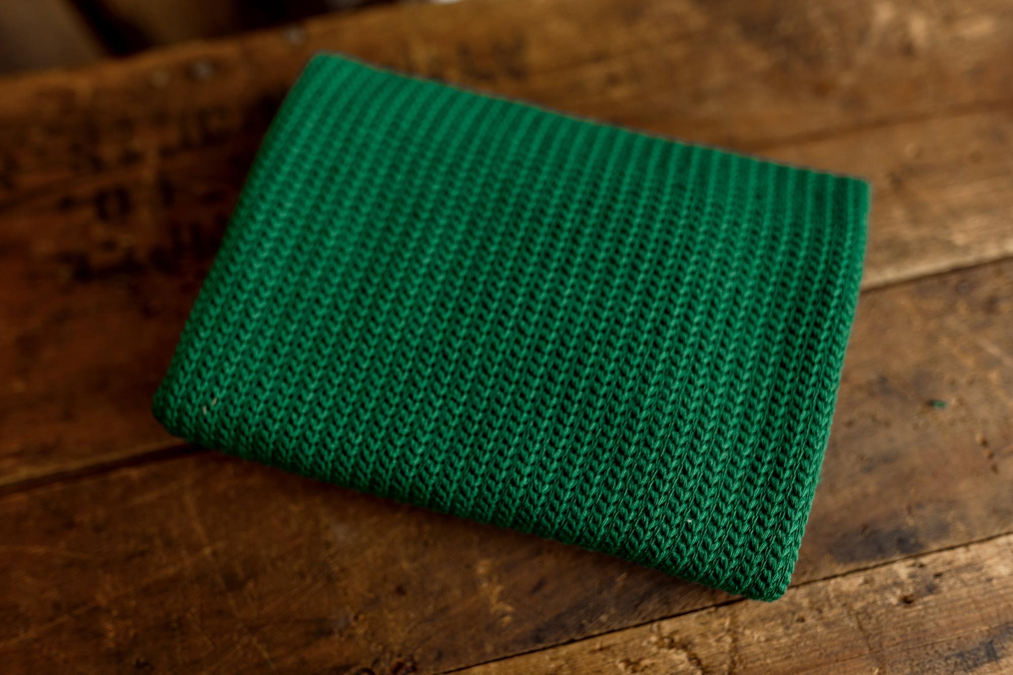 Folded deep evergreen stretch knit newborn photography wrap with a textured pattern on a rustic wooden surface.