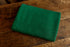 Folded deep evergreen stretch knit newborn photography wrap with a textured pattern on a rustic wooden surface.