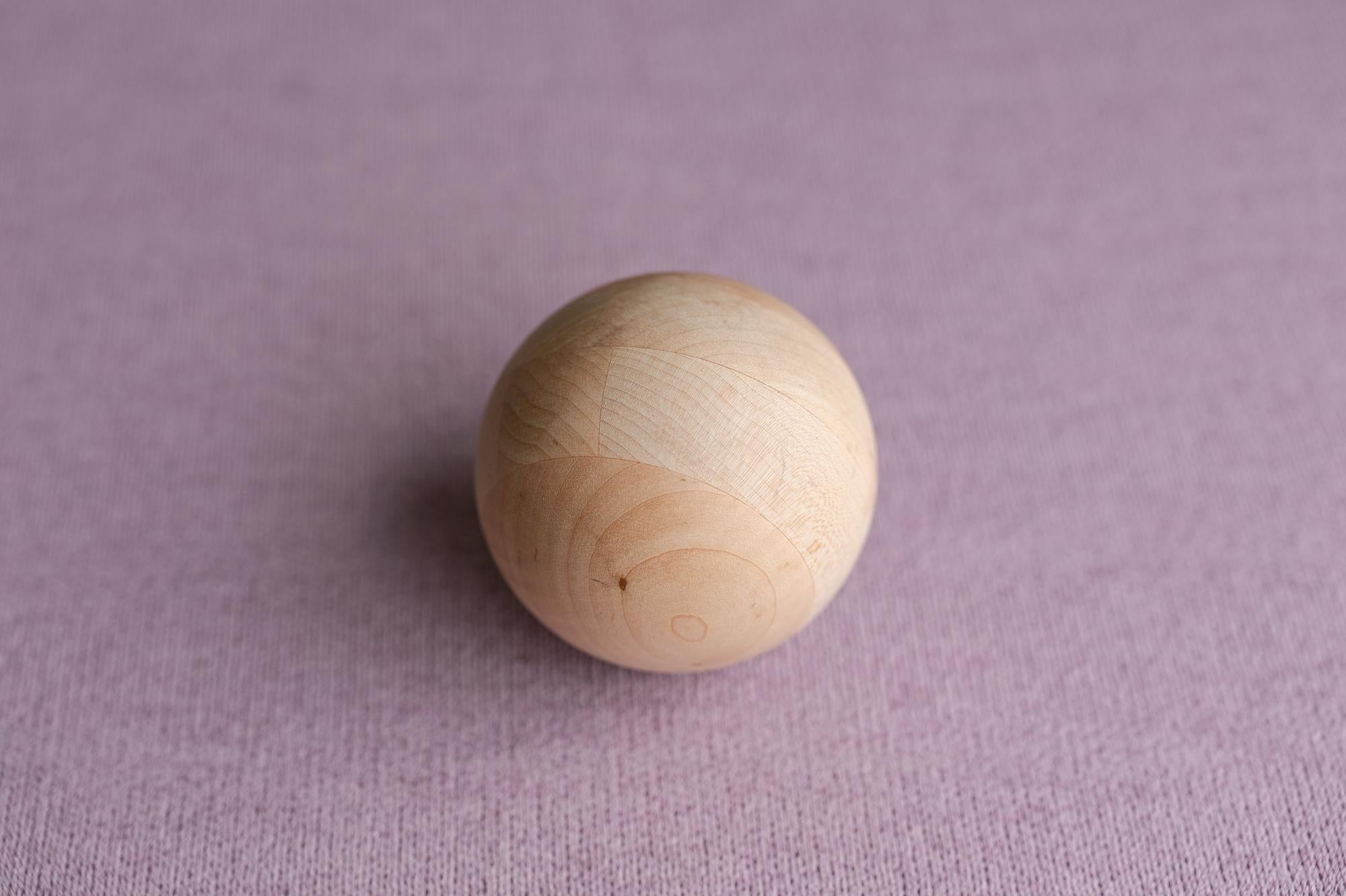 Smooth wooden sphere resting on a textured, muted lavender Nest fabric backdrop for newborn photography.