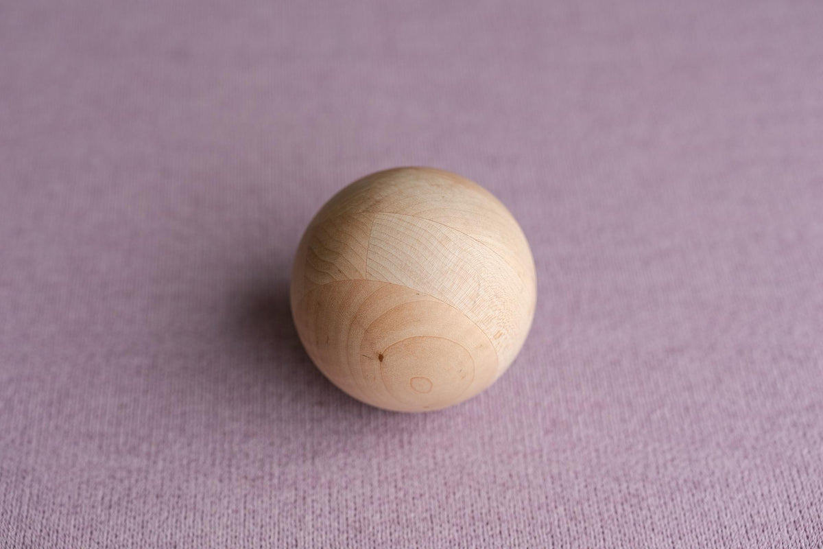 Smooth wooden sphere resting on a textured, muted lavender Nest fabric backdrop for newborn photography.