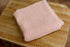 Soft, strawberry milk pink newborn photography wrap with a textured, open-knit design folded on a wooden surface.