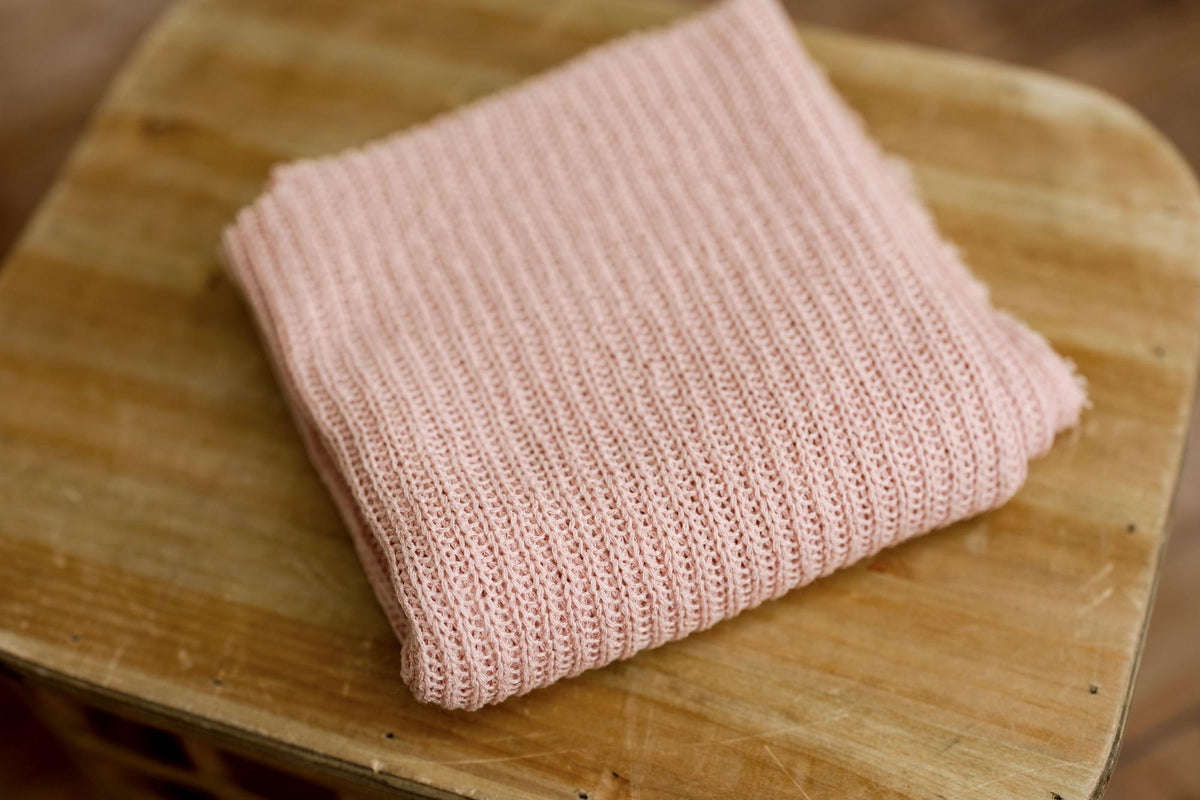 Soft, strawberry milk pink newborn photography wrap with a textured, open-knit design folded on a wooden surface.