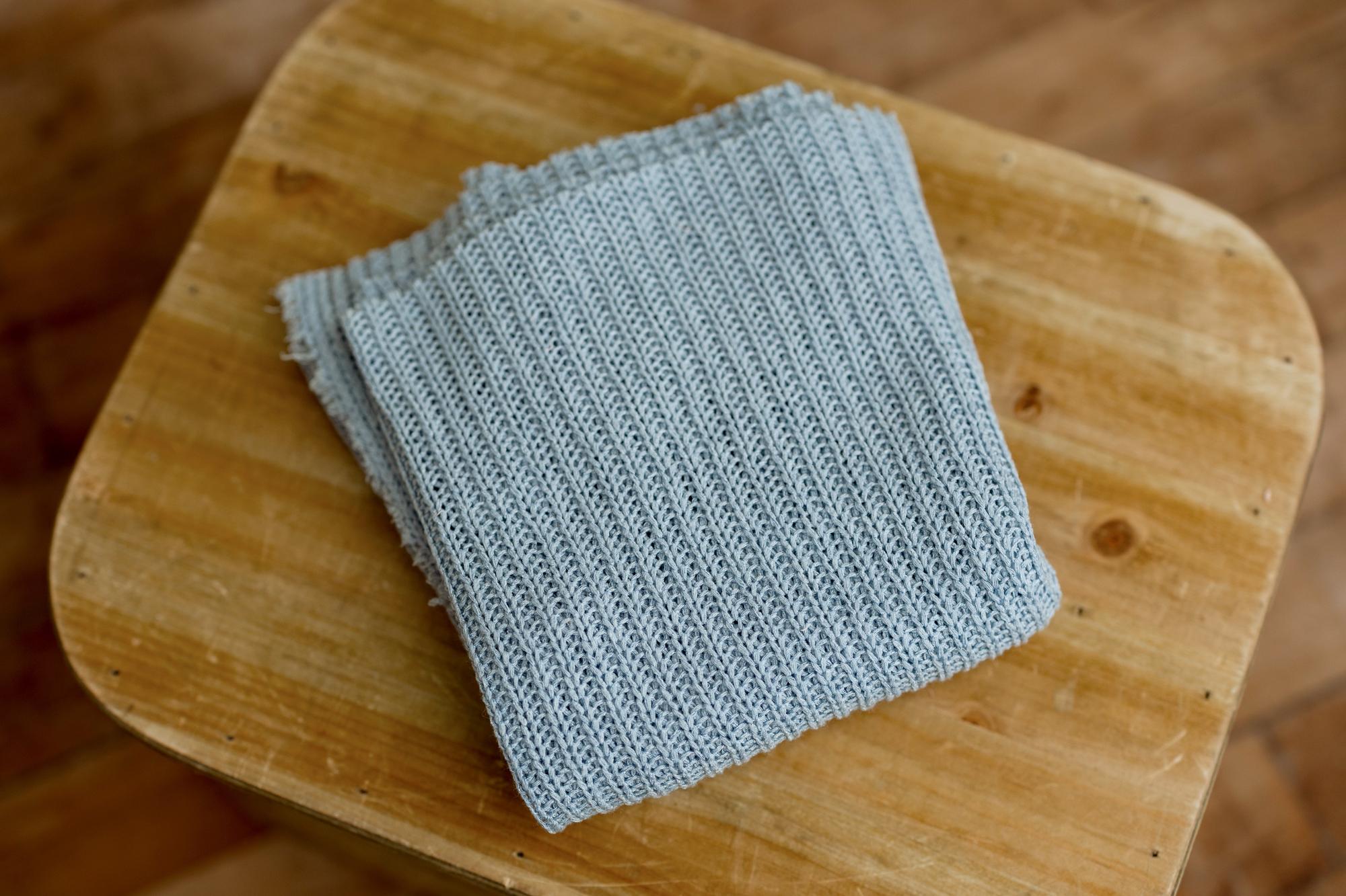 Smurf blue newborn photography wrap with a soft, open-knit texture and frayed edges, folded on a wooden surface.