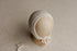 Neutral beige newborn photography bonnet with a delicate textured trim and tie strings on a mannequin head.
