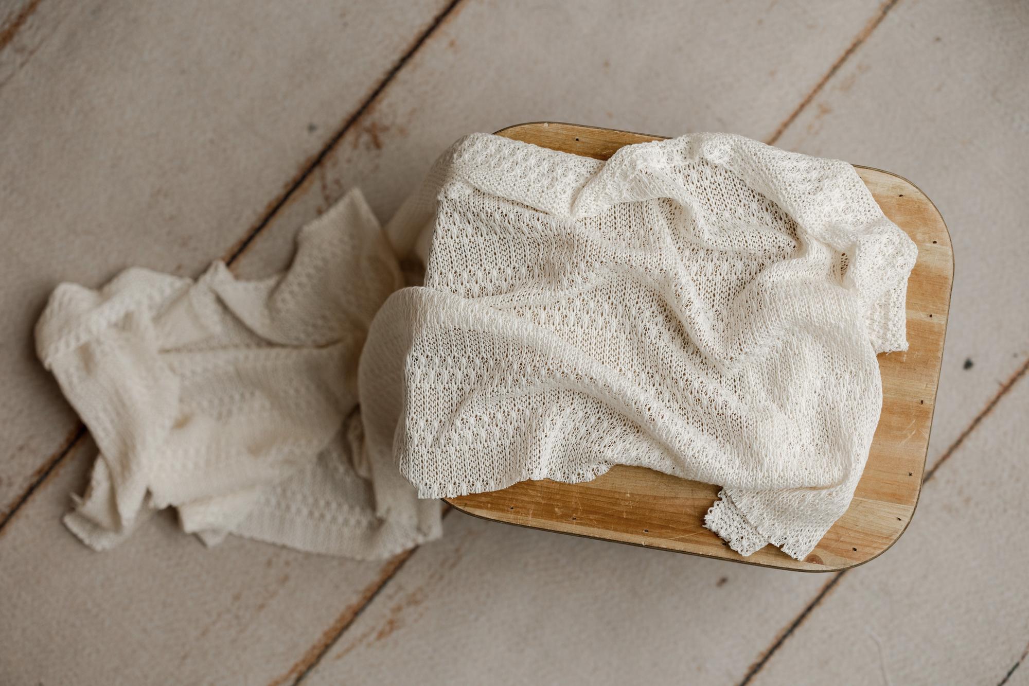 Soft ivory open-knit fabric draped over a wooden prop for newborn photography sessions.