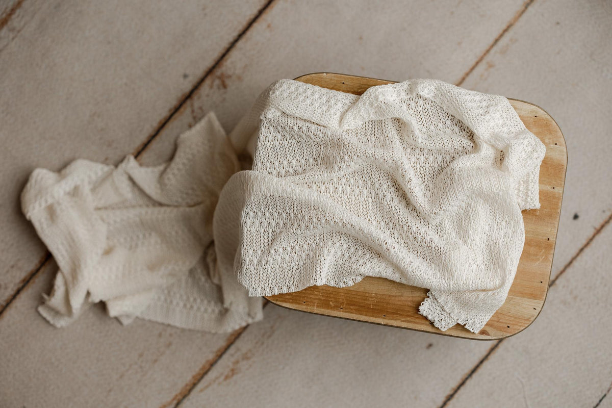Soft ivory open-knit fabric draped over a wooden prop for newborn photography sessions.