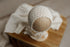 Ivory newborn photography bonnet and matching open-knit fabric wrap on a wooden display stand.
