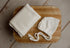 Ivory open-knit newborn posing fabric wrap and matching bonnet set on a rustic wooden surface.