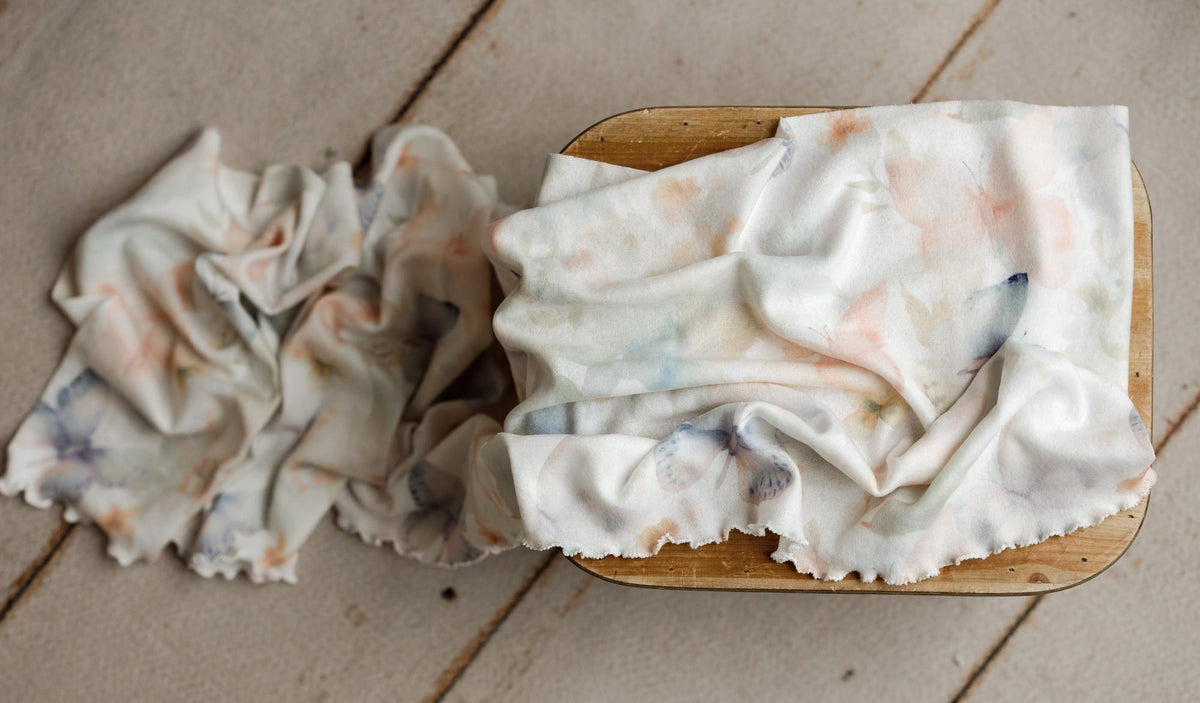 Soft white newborn posing fabric and ruffle wrap with delicate watercolor butterfly print on a wooden stool.