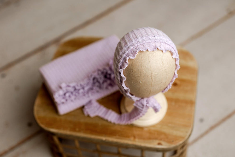 Lavender lilac brushed waffle knit newborn photography wrap and matching ruffled bonnet on a wooden display.