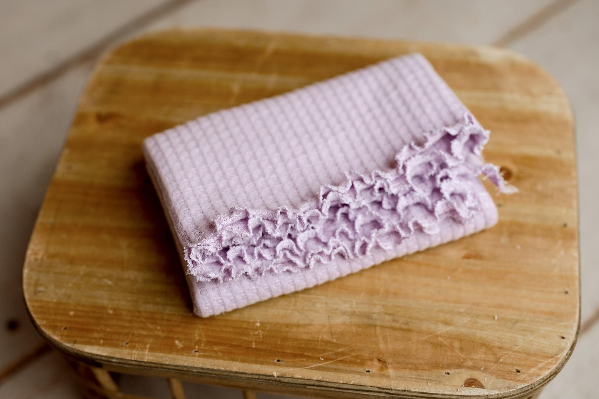 Lavender lilac newborn photography wrap in soft waffle knit fabric with delicate ruffled edging on a wooden surface.