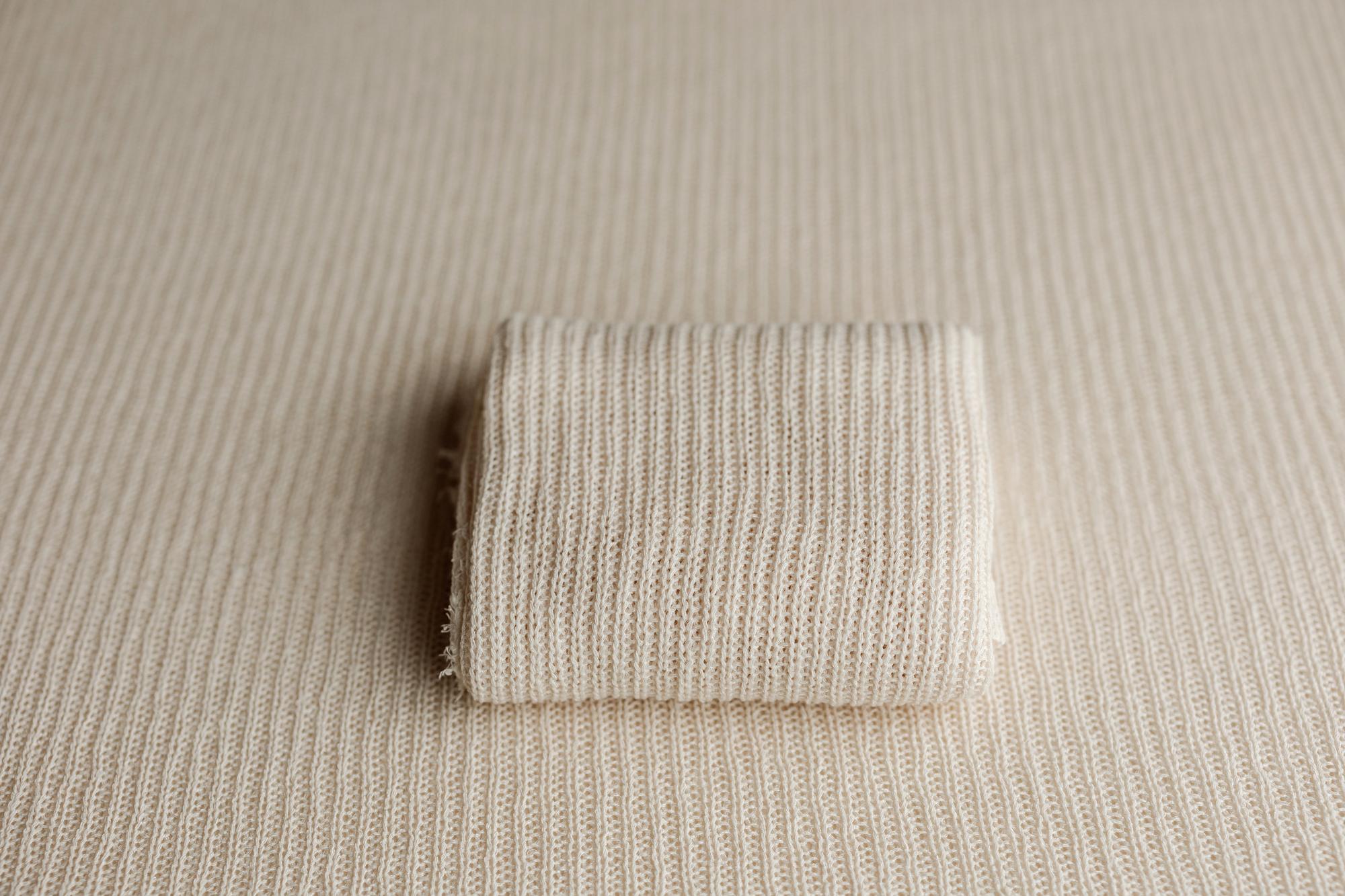 Beige ramen-toned newborn photography fabric wrap with a soft, open-knit texture folded on a matching posing base.