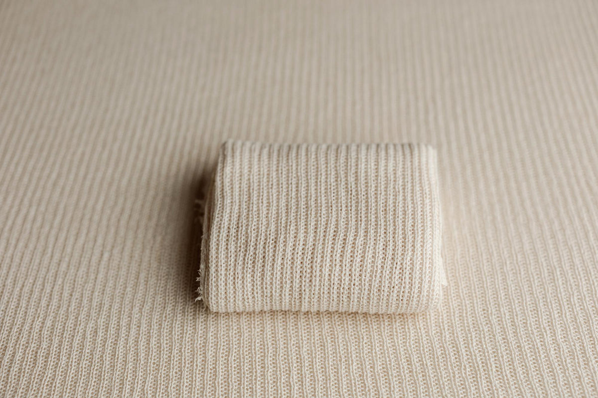 Beige ramen-toned newborn photography fabric wrap with a soft, open-knit texture folded on a matching posing base.