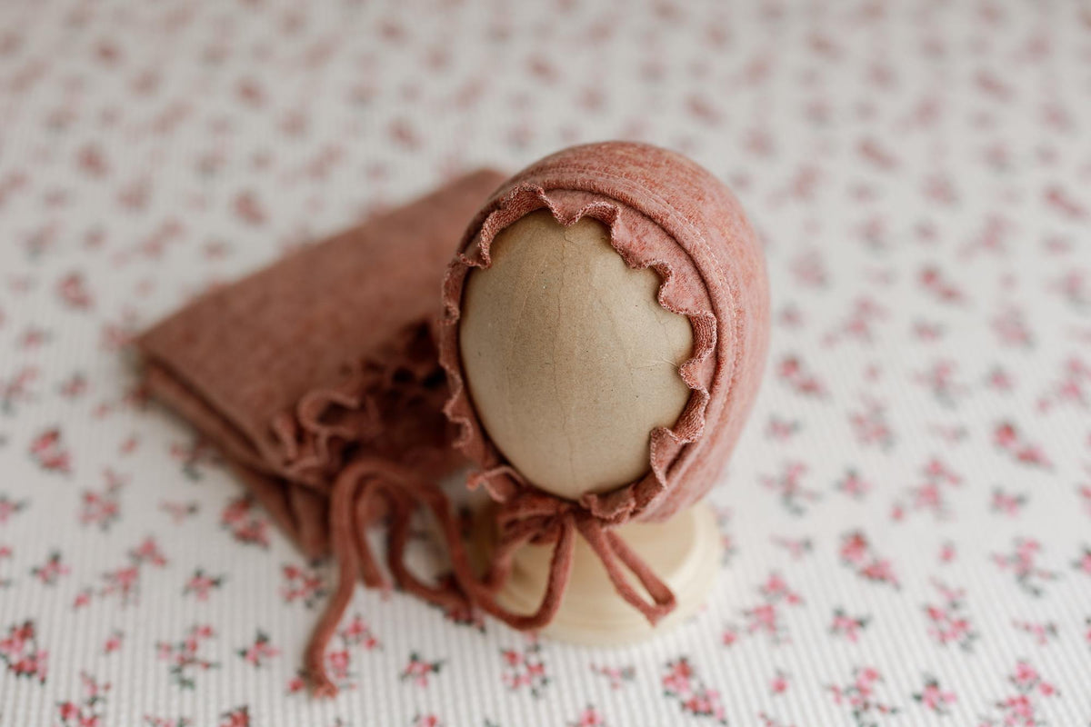 Primrose pink floral newborn backdrop with a matching textured ruffle wrap and bonnet on a display stand.