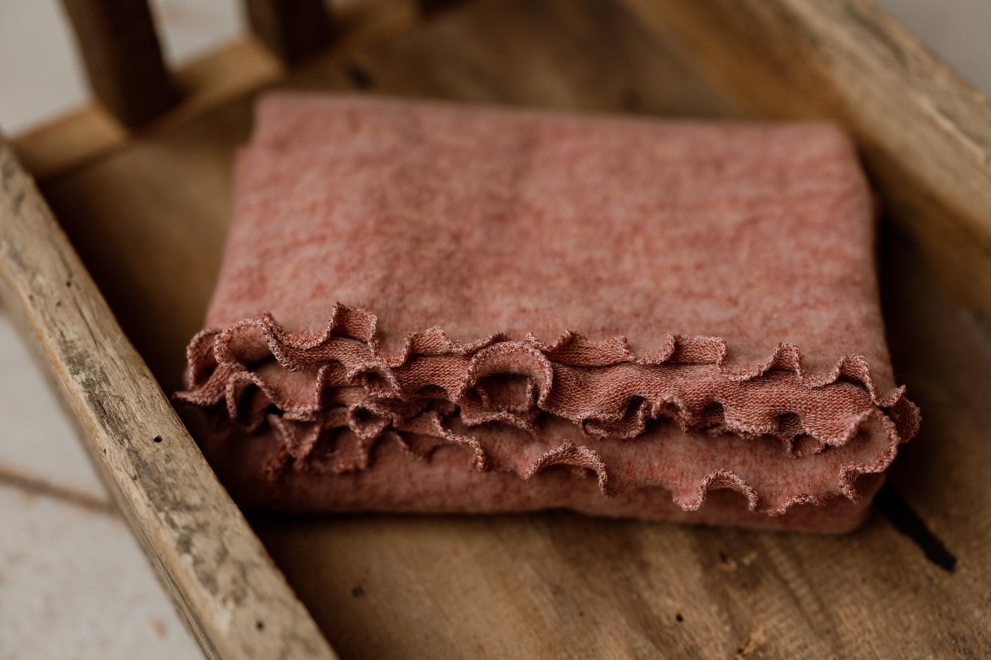 Primrose pink floral textured newborn photography wrap with delicate ruffle trim, folded inside a rustic wooden prop.